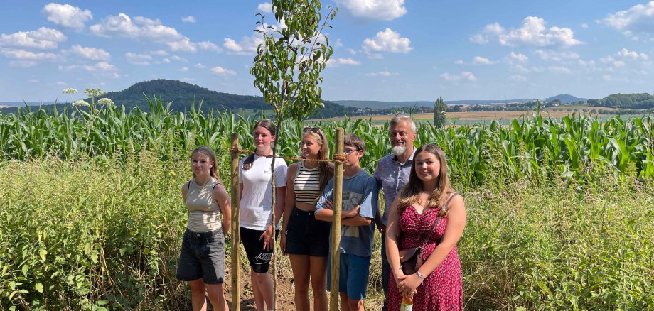 Jugendliche und Betreuer vor einem frisch gepflanzten Baum.